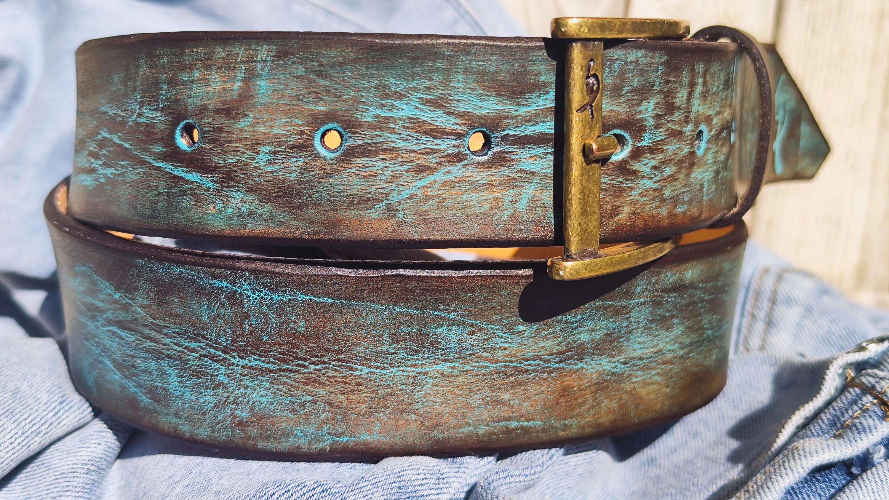 Artisan leather belt with blue-green patina laid on light blue jeans