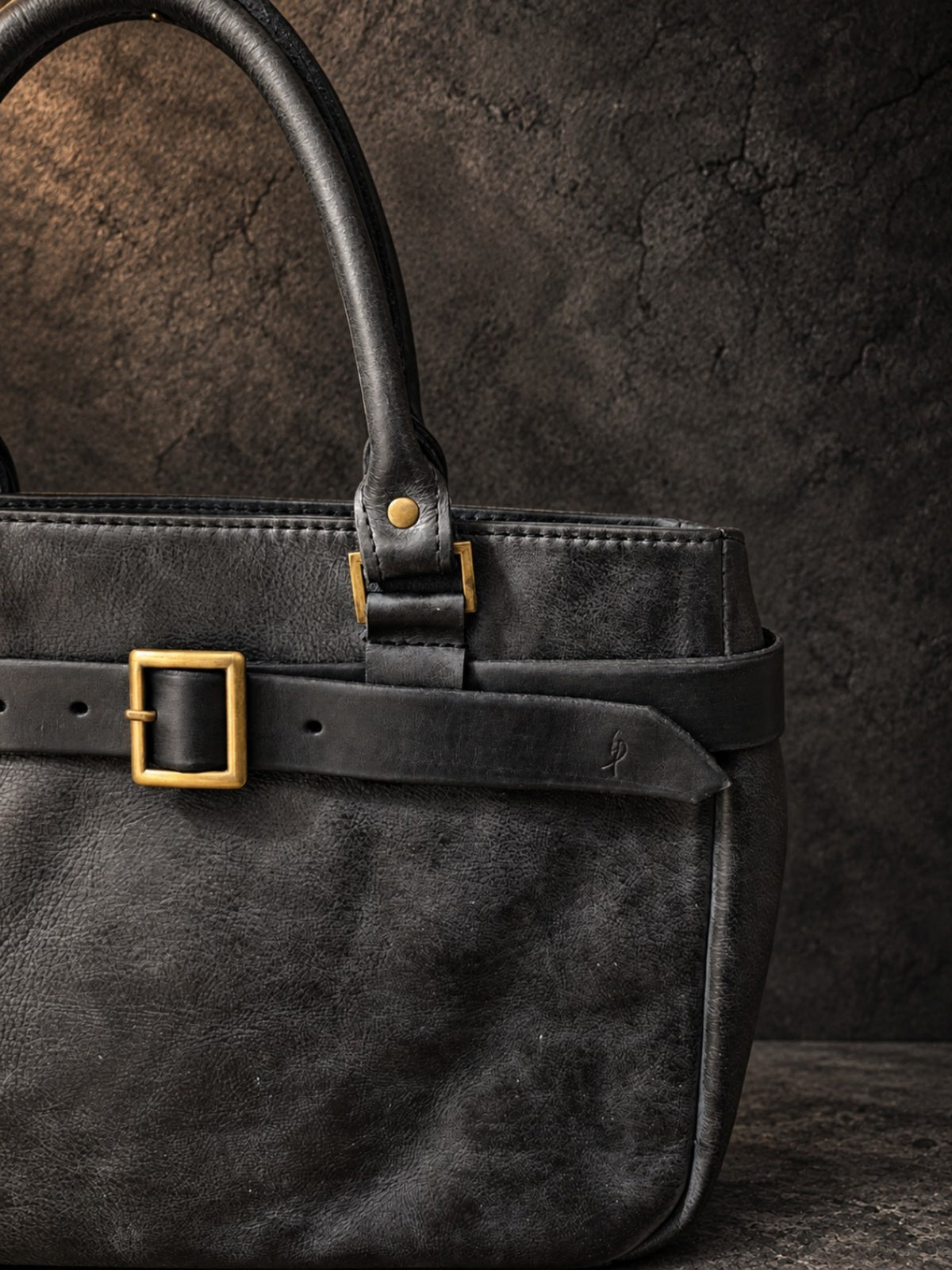 Detail of hand-dyed black leather texture, handle and brass hardware on ISHAOR handbag