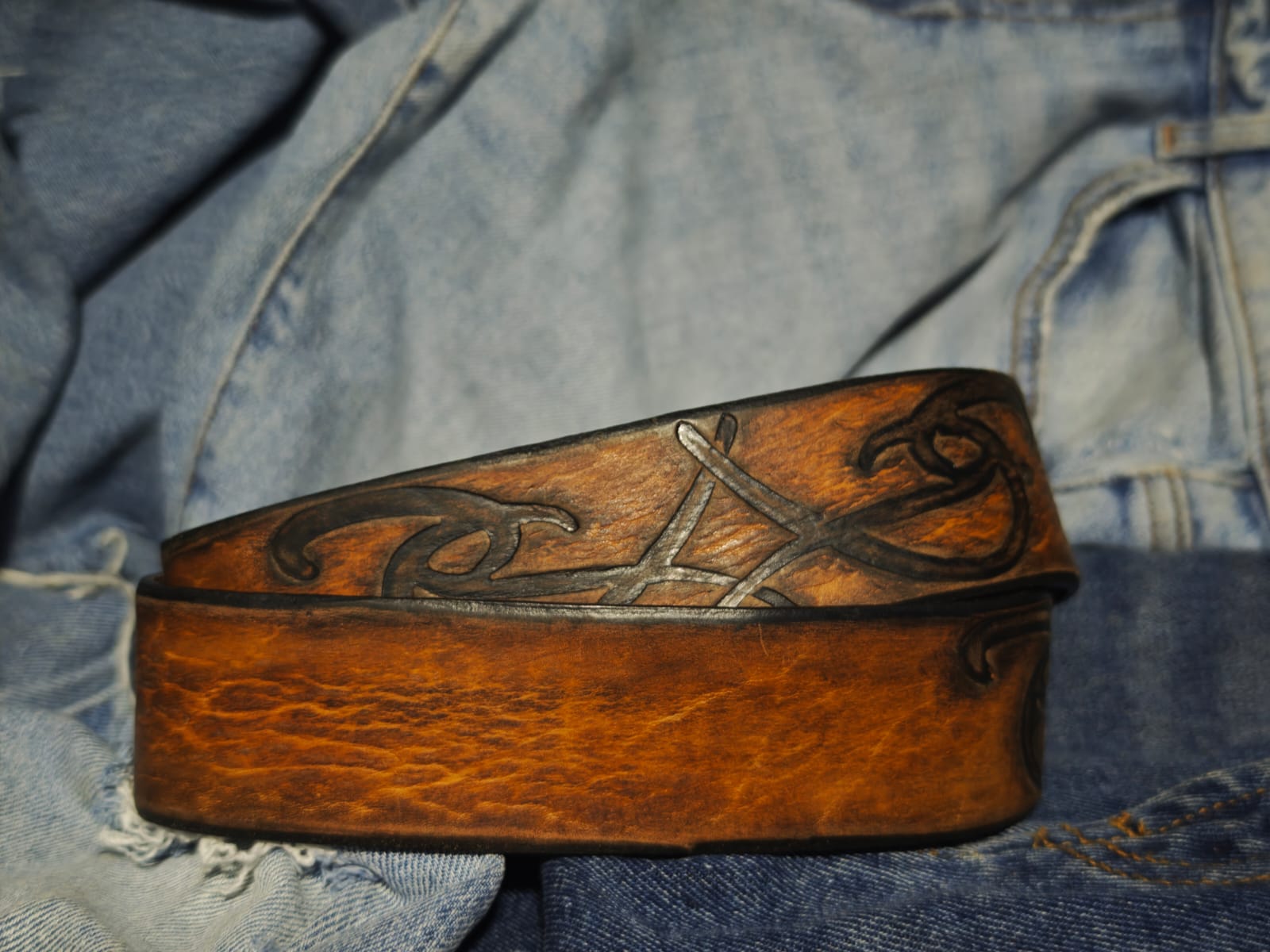 Brown leather belt with a metal buckle embossed with a unique decorative pattern