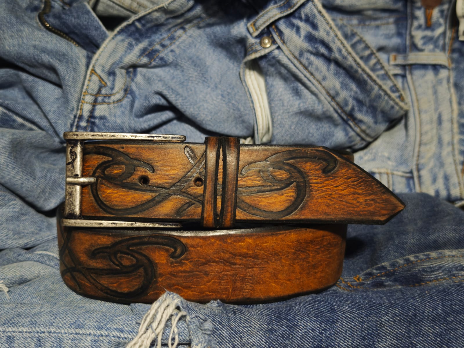 Brown leather belt with a metal buckle embossed with a unique decorative pattern