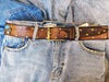 Brown leather belt with two shades of brown two pieces on the front and storage for guitar pick with bronze studs around the belt